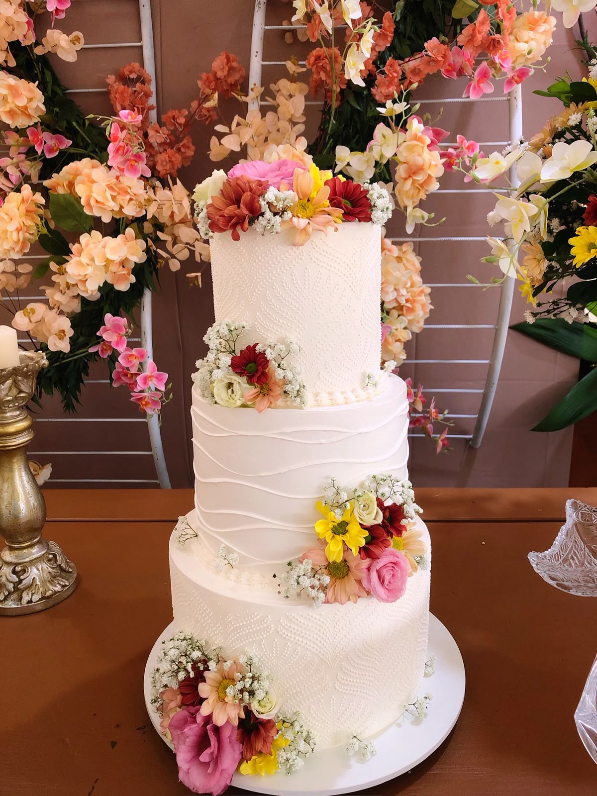Bolo de casamento de três andares coberto de flores naturais coloridas