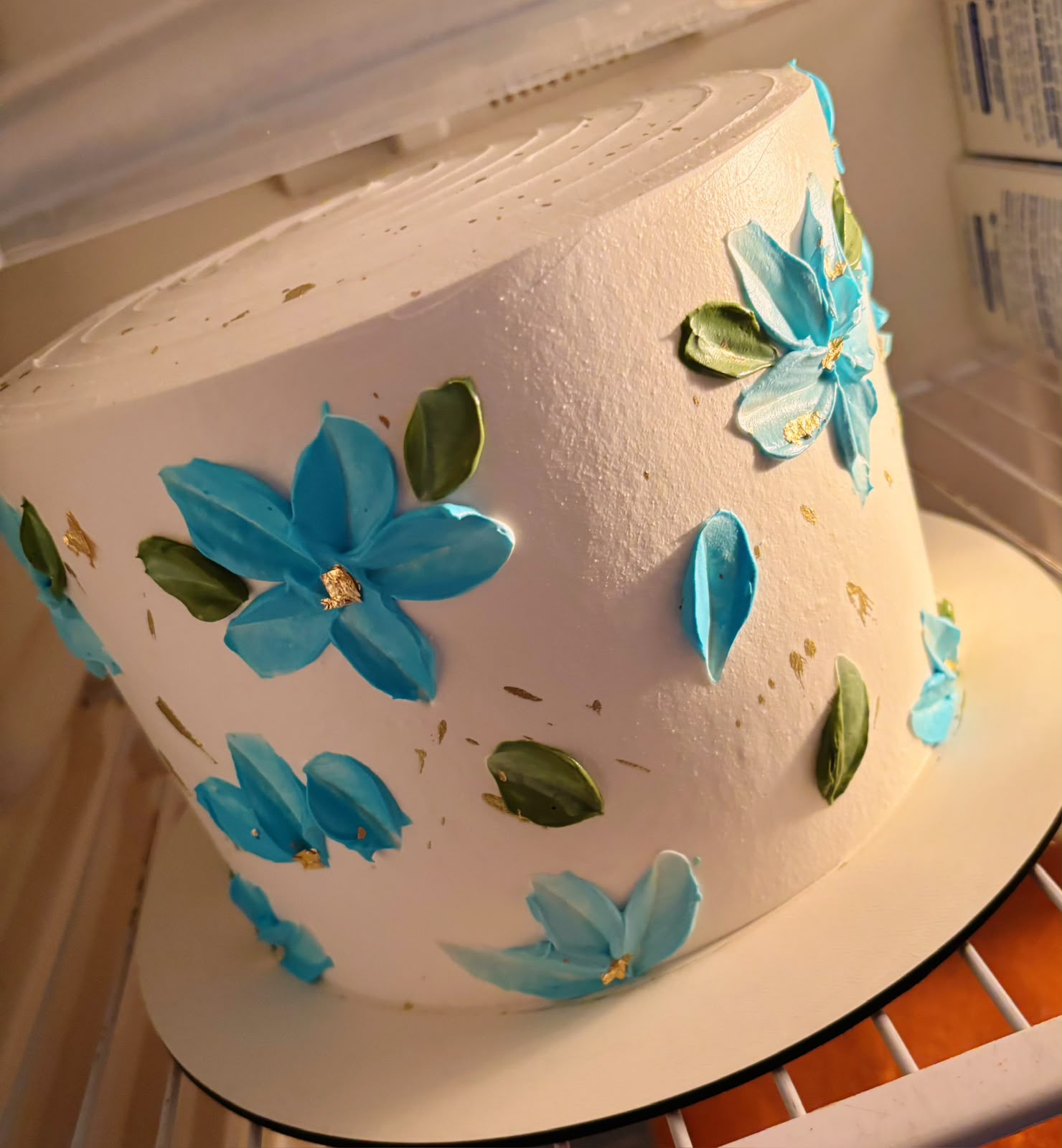 Bolo branco com flores azuis pintadas em espátula e detalhes em folha de ouro